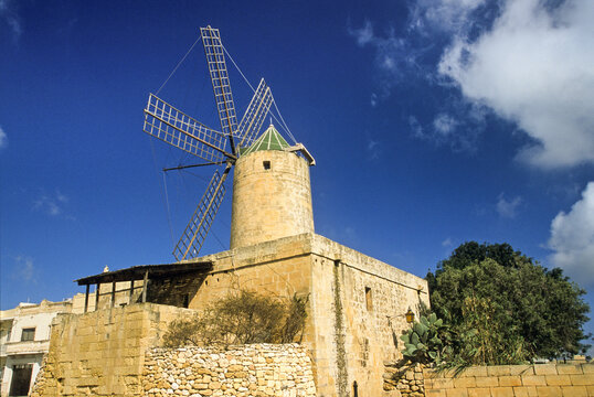Ancient windmill TaKola stands in Xaghra under a clear sky in Gozo, Malta surrounded by stone walls and greenery