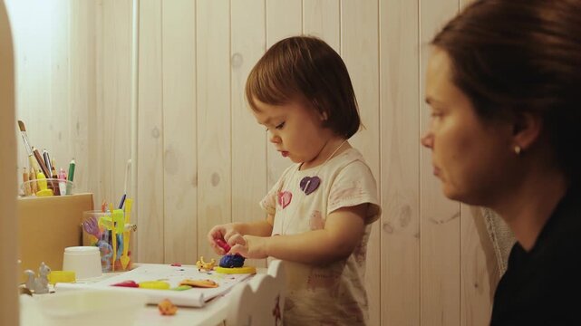Young child enjoys a calm creative moment with colorful clay while spending time beside her mother.