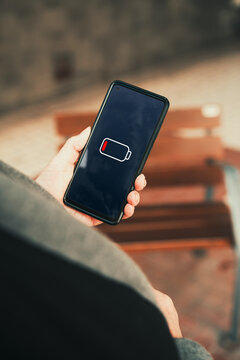 Low battery warning icon on smartphone screen held by mature woman hand. battery anxiety, technology dependency, and power management issues concepts.