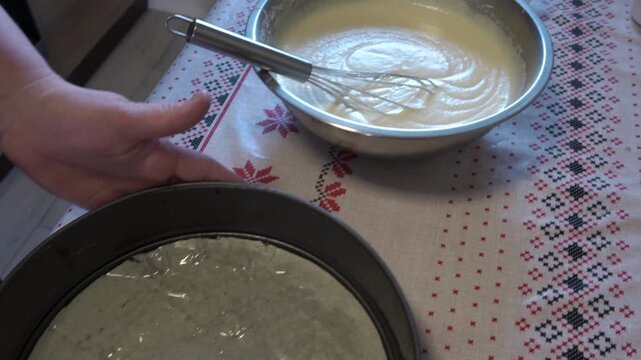 Pouring raw liquid batter from a bowl into a metal baking pan, Process of pouring biscuit batter or cream into a pan close up