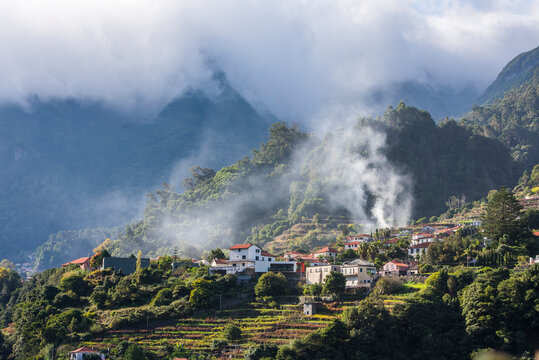 Mist and smoke surround houses in a village in Madeira during a cloudy day near the coast of Portugal