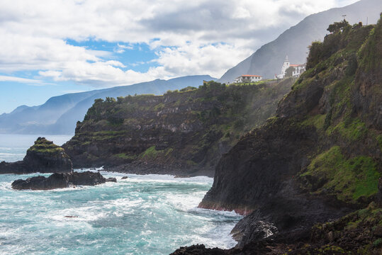 Coastline with rocky cliffs and ocean waves near Seixal in Madeira, Portugal on a clear day with clouds in the sky