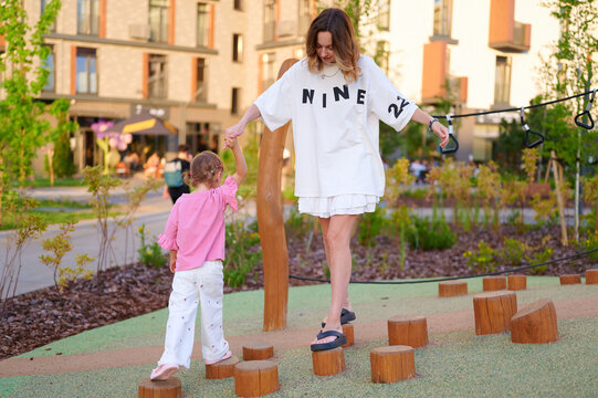Mother and daughter holding hands while balancing on wooden stumps at a modern playground