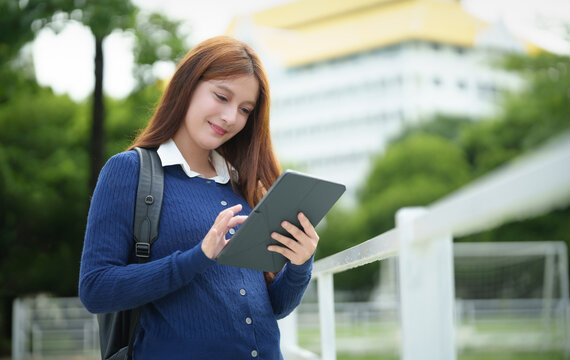 Female student uses a digital tablet on a university campus, enjoying modern mobile learning, online connectivity, and academic life outdoors.