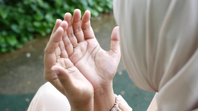 Close up of muslim woman in hijab praying outdoors with hands raised to sky during ramadan, slow motion footage