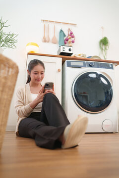 Woman relaxes with a smartphone while waiting for laundry, combining smart home convenience, digital connectivity, and efficient everyday household living.