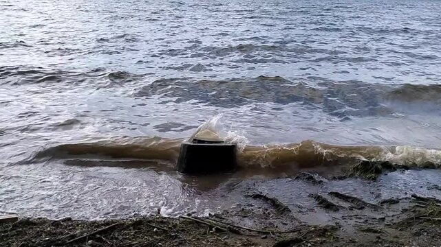 Lake waves crashing over a weathered tree stump on a muddy shoreline, representing water level changes, soil erosion, and moody nature backgrounds