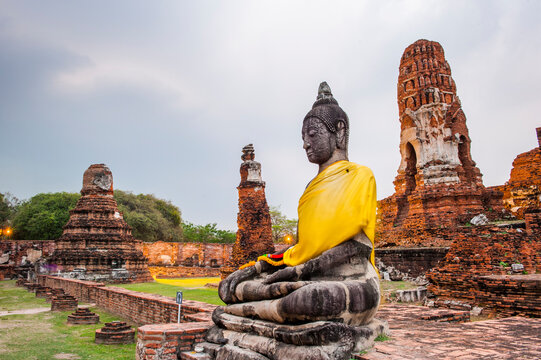 Sitting Buddha in Wat Mahathat with ancient ruins and stone structures at sunset in Ayutthaya Thailand