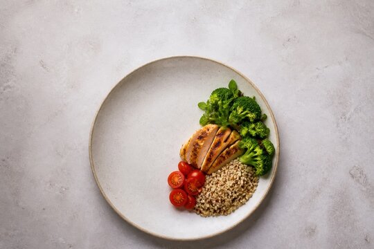 Grilled chicken with broccoli, quinoa, and tomatoes on a plate, top view of a healthy meal.