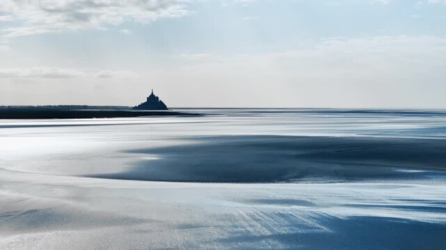 Broad bay at low tide on Normandy coast with natural shoreline patterns, wet sand surfaces and shallow tidal channels