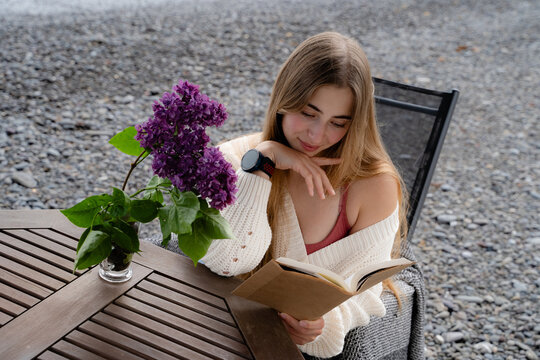 Young woman absorbed in a paper book while relaxing beside the ocean. Mindfulness, digital detox and quiet seaside recreation concept.