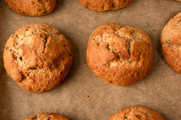 Naklejka premium A top-down view shows golden-brown oatmeal cookies with cracked, rustic surfaces arranged neatly on parchment paper, evoking a warm, homemade feel.