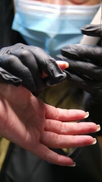 A woman's hand during a manicure. A woman getting a manicure. A manicurist is doing a client's nails at a nail salon. Manicure services - Vertical video