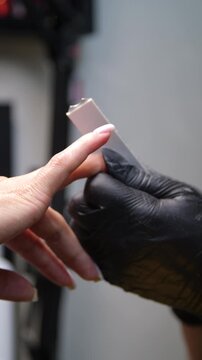 A woman's hand during a manicure. A woman getting a manicure. A manicurist is doing a client's nails at a nail salon. Manicure services - Vertical video