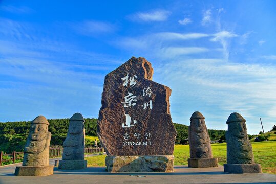 Exploring Songaksan with stone statues and a large rock sign on a sunny day in Jeju Island, South Korea