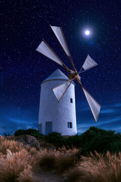 Historic white windmill at night with a glowing moon and starry sky, photorealistic 8k detail