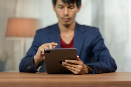 Young man in formal attire sitting at wooden desk using smartphone in modern indoor setting