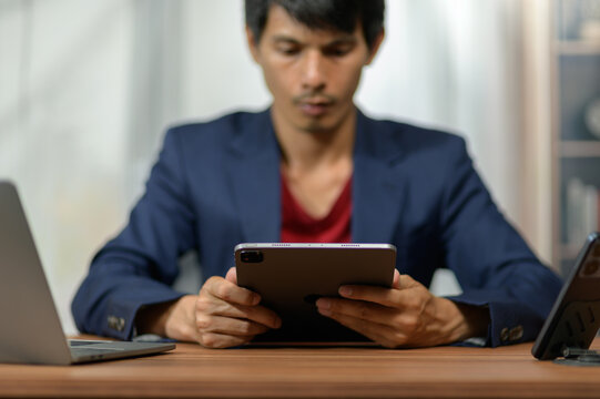 Young Man Using Tablet Computer at Office Desk with Laptop and Smartphone