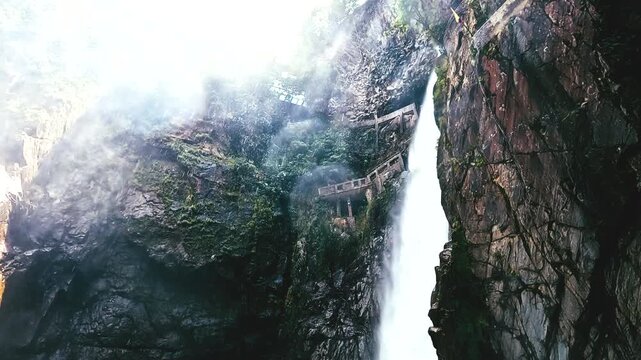Tall Waterfall Dropping Into Narrow Rocky Gorge in Ecuador with Mist, Canyon Bridge, Green Vegetation and Scenic Adventure Travel Scene