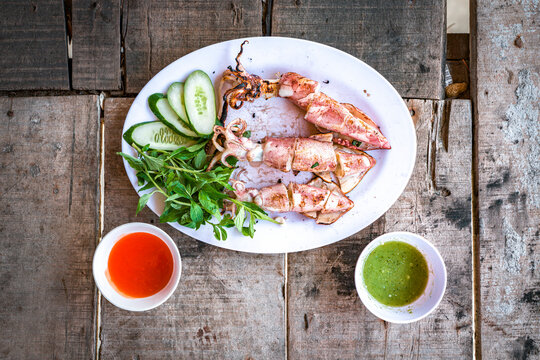 Grilled squid served with herbs and sauces on a wooden table in Vietnam for a traditional dining experience