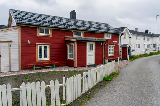 Red wooden house on a quiet road beside white buildings in Veiholmen, Smola Municipality, Vestland, Norway