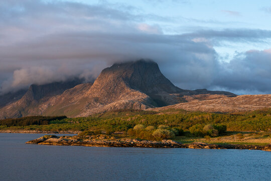 View of mountain with clouds over the peak near a coastline in Nordland during a sunset in late summer