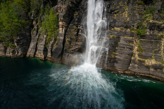 Waterfall flows down rocky cliffs into clear waters in Melfjord, Svartisen National Park, Norway during daylight hours