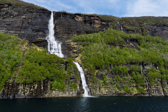 Waterfalls flow down rocky cliffs surrounded by green trees in Melfjord, Svartisen National Park in Norway
