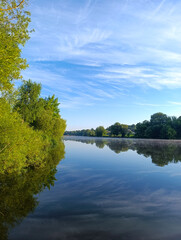 Obraz premium Beautiful reflection of blue sky and wispy clouds in a calm river surrounded by green trees