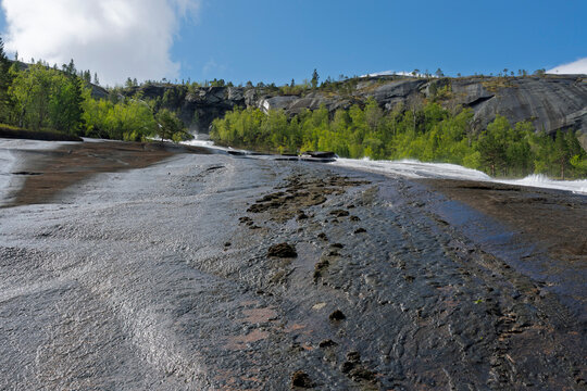 View of flat rock surface leading to forest near Tysfjorden with blue sky and clouds above, showcasing natural landscape in Norway