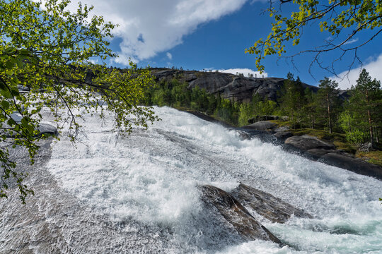 View of rushing water over rocky terrain surrounded by trees in Tysfjorden area of Norway