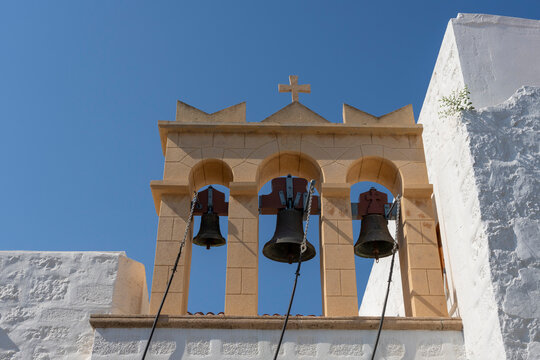 Church bells ring at Agios Nikolaos in Skala, capturing daily life in Patmos, Greece during bright sunny hours with clear blue sky
