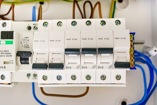 Macro view of modern circuit breakers in an electrical panel. Close-up of automatic safety switches with technical symbols and indicators in domestic consumer unit fuse box.