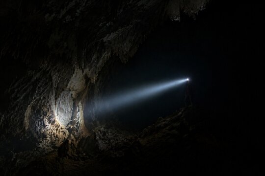A single beam of light from a helmet lamp illuminates a dark cave.
