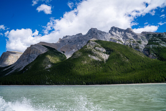 Boat wake splashes across the turquoise waters of Lake Minnewanka beneath rugged limestone peaks in Banff National Park, Alberta, Canada.