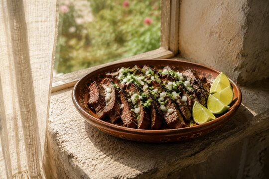 taqueria. Clay dish of grilled carne asada with cilantro, onion, and lime on stone ledge, authentic Mexican taco filling and food presentation concept, menu design.