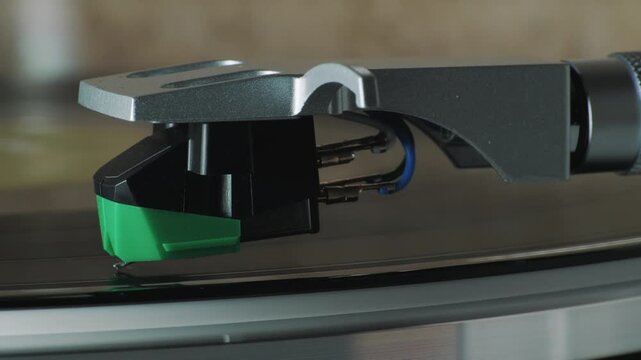 Phono cartridge tracking vinyl LP groove on turntable, side view of tonearm and stylus during analog playback, macro detail, hi-fi audio equipment, shallow depth of field.