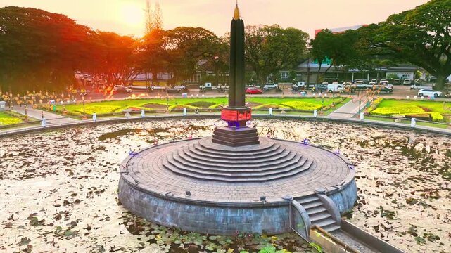 Golden hour bathes historic building and central monument. Circular pond reflects sky and structure. Lush greenery surrounds the scene. Distant trees frame the peaceful vista