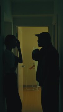 Asian couple having a fierce argument in a dark hallway at home. Concept of relationship conflict, communication breakdown and marriage crisis. Vertical Shot