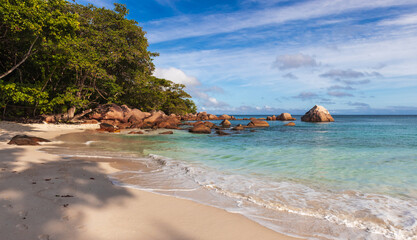 Obraz premium Anse Lazio, Praslin, Seychelles. Vibrant tropical beach featuring calm azure waters, large rock formations, and trees providing shade under a sunny blue sky