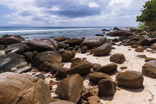 Tropical beach scene featuring large boulders and ocean water under bright blue skies. Calm, relaxing, and picturesque coastline setting of Beau Vallon, Seychelles
