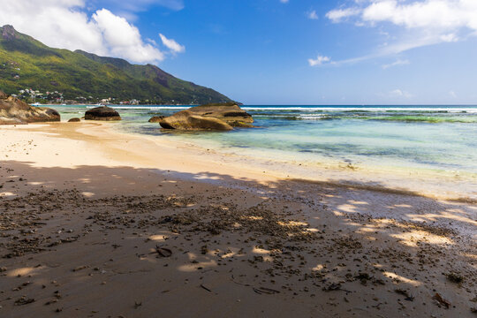 Beau Vallon Beach, Seychelles. Coastal landscape with white sand, wet stones and distant coastal mountains under bright blue sky on a sunny day