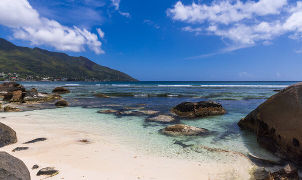 Coastal view of Beau Vallon beach, Seychelles with clear turquoise water, black rocks and blue sky creates a panoramic scenic resort scene