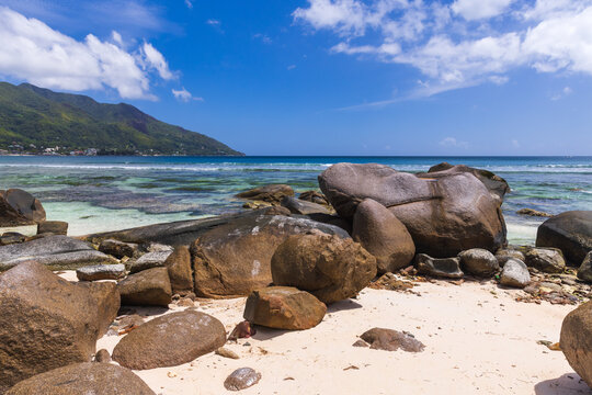 Beau Vallon, Seychelles, rocky beach view with clear turquoise water, scattered boulders, and vibrant blue sky creates a scenic view. 