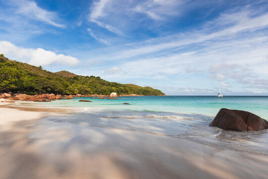 Anse Lazio beach, wide white sandy shore is under partly cloudy blue sky on a sunny day. Coastal landscape of Praslin island, Seychelles