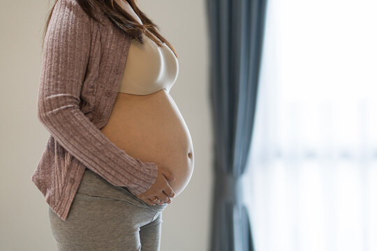 Side view close-up of a standing pregnant woman gently holding her bare belly.