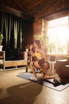 Woman performing kneeling lunge with resistance band during home workout. Concept of glute activation, mobility training, lower body strength and rehabilitation exercise.