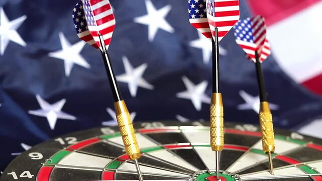 Patriotic darts featuring the American flag design are stuck firmly in the center of a board while a United States flag waves in the background during a holiday celebration held on July 4th