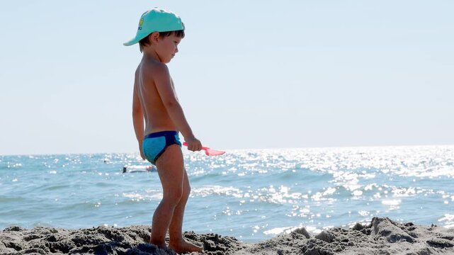 Little Boy Playing on Sandy Beach with Shovel on Sunny Day