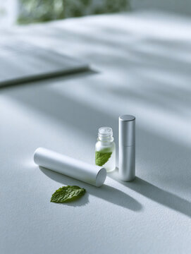 Nasal inhaler peppermint oil mint leaf still life white cylinder glass bottle aromatherapy minimal composition gray background soft shadow